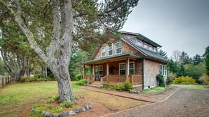 A two-story house with a porch, surrounded by a well-maintained lawn and trees. - Historic District Home - Walk to Willapa Bay! (Oysterville)