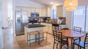 A modern kitchen with white cabinets, a stainless steel refrigerator, a microwave, and a large island with bar stools. - Perfectly-Located, Charming Family Home w/ Pool (Phoenix)