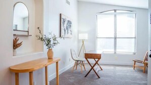 A modern living room with a wooden console table, a floor lamp, and a large window with blinds. - Perfectly-Located, Charming Family Home w/ Pool (Phoenix)