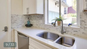 Une cuisine dotée d’un évier à deux bacs, de meubles blancs, d’une fenêtre offrant une belle vue et d’un crédence ornée d’un motif en mosaïque.