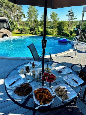 A poolside dining area with a table set for a meal, surrounded by a pool and greenery.