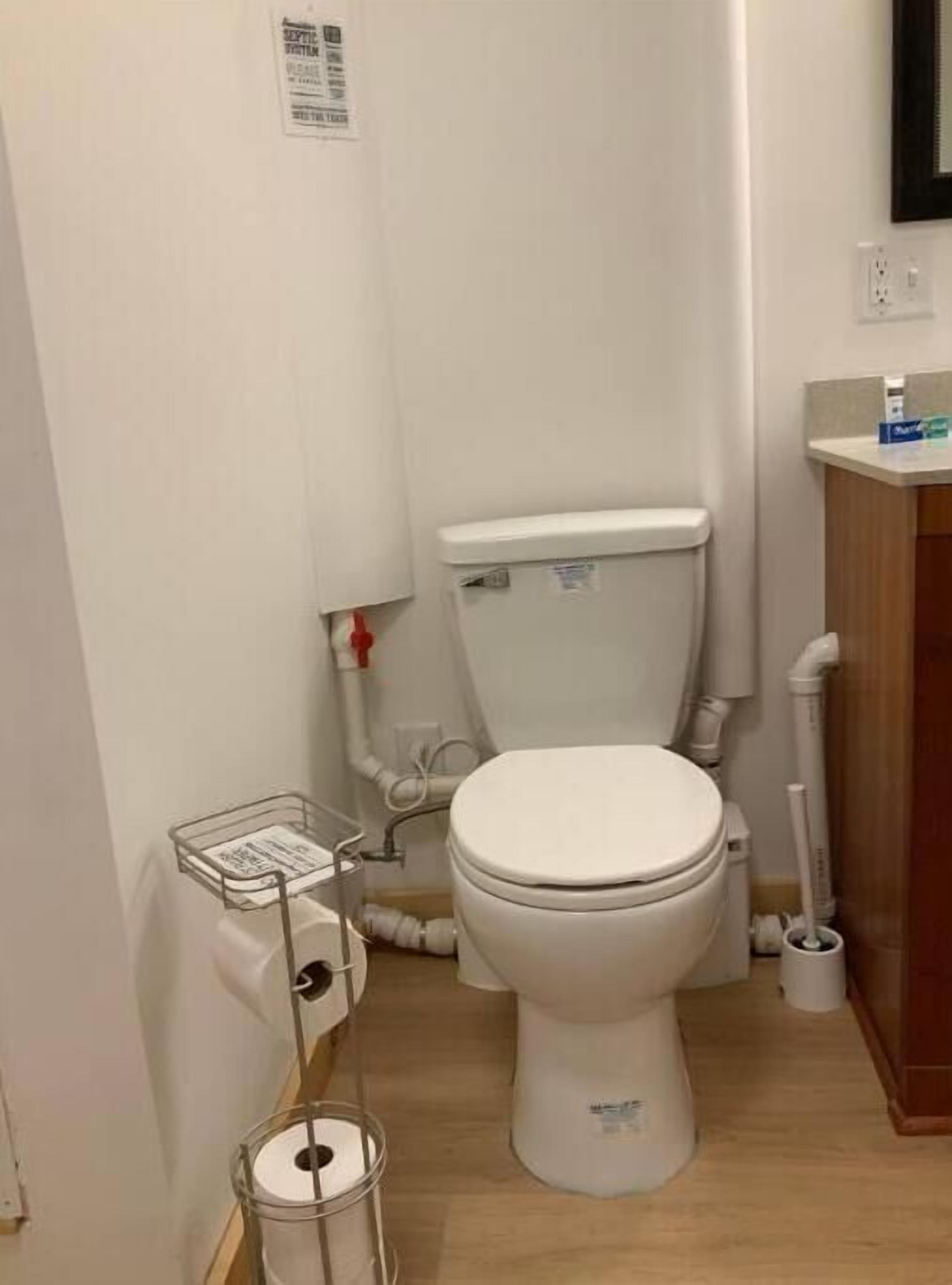 Een kleine, schone badkamer met toilet, een metalen prullenbak en een houten kastje.