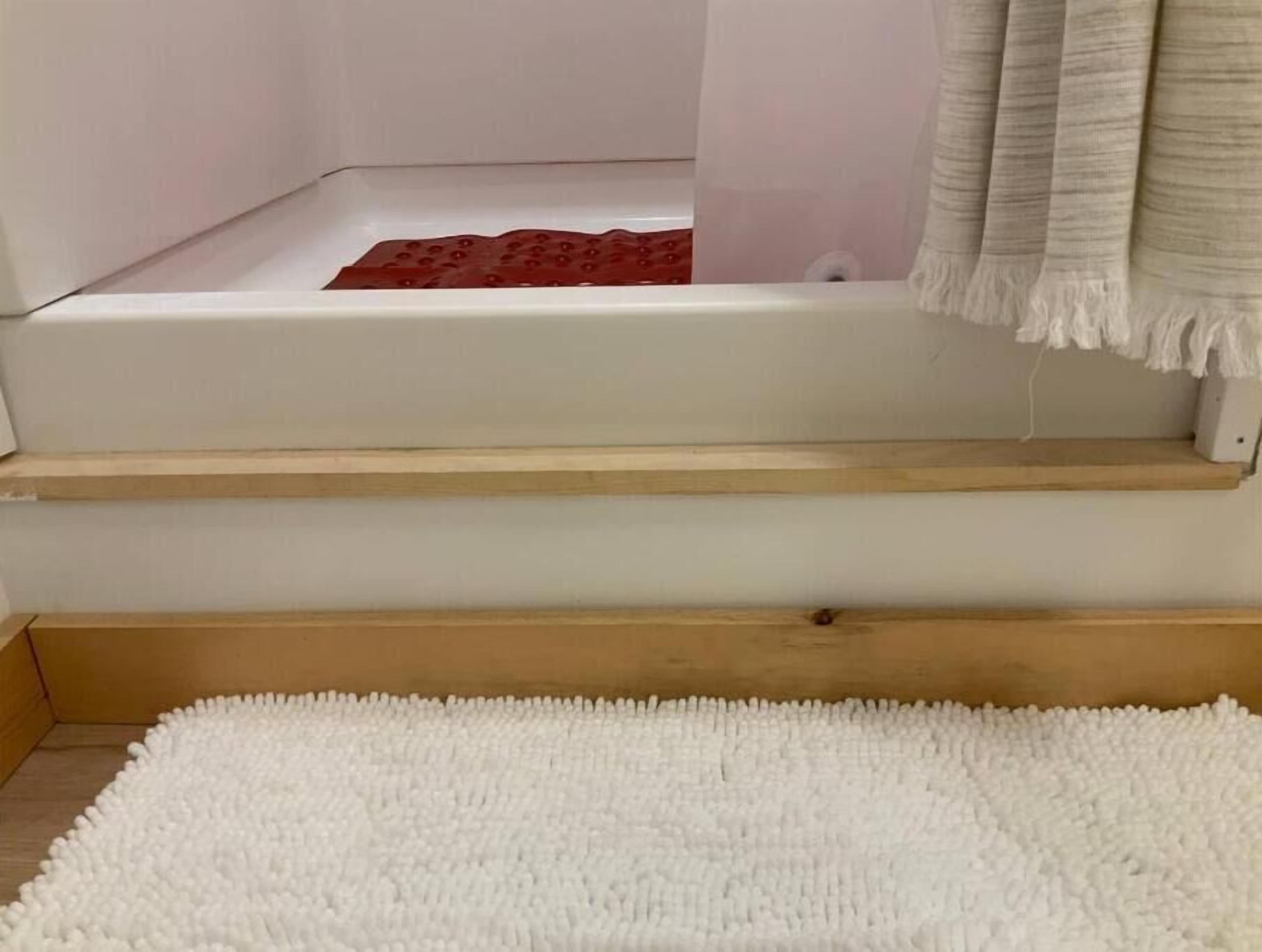 A room with a white textured rug, a wooden shelf, and a red object on the floor.