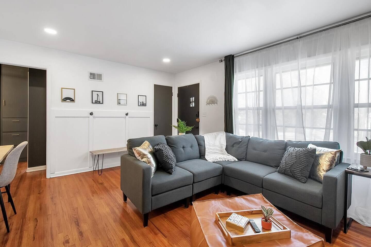 Un salon moderne avec un canapé d’angle gris, une table basse en bois et un coin repas comprenant une chaise et une table.