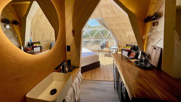 A cozy, triangular tent-style room with a bed, a sink, and a dining area.