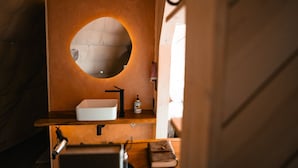 A bathroom with a round mirror, a white sink, and a wooden vanity.