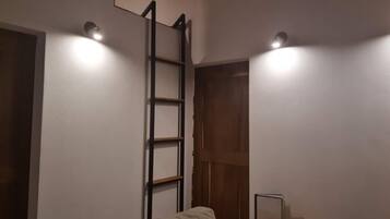 Una habitación con sofá, una escalera de madera y dos luces fijadas a la pared.