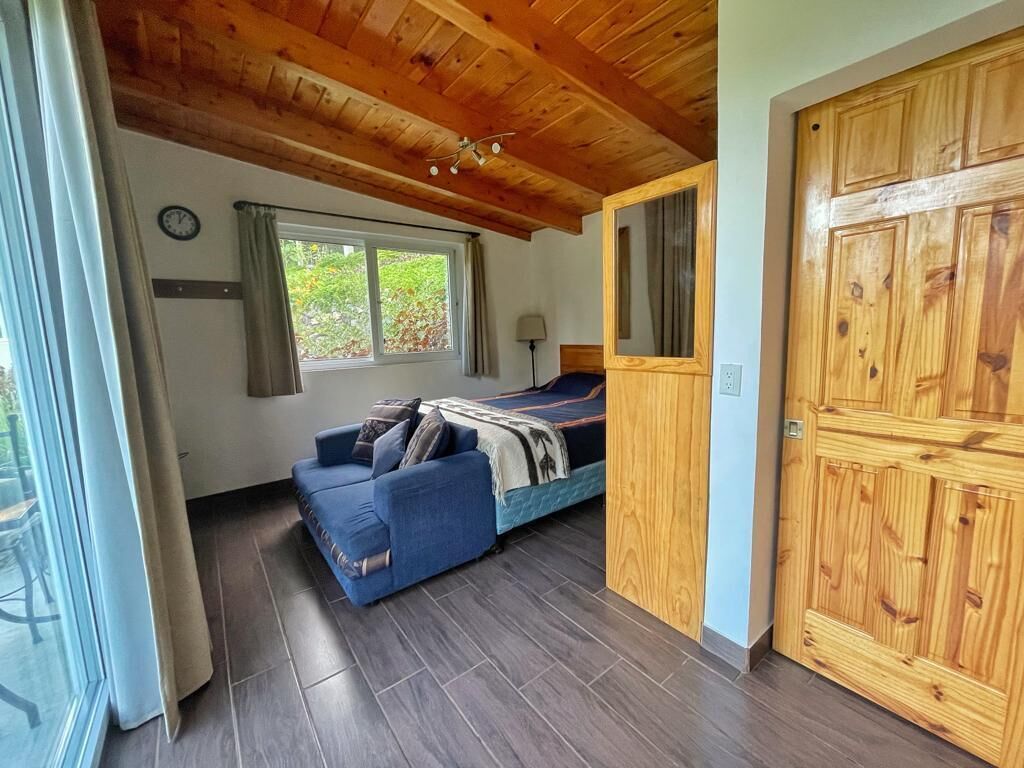Une pièce comprenant un lit, un canapé bleu, une armoire en bois et une fenêtre avec des rideaux.