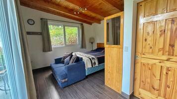 Une pièce comprenant un lit, un canapé bleu, une armoire en bois et une fenêtre avec des rideaux.