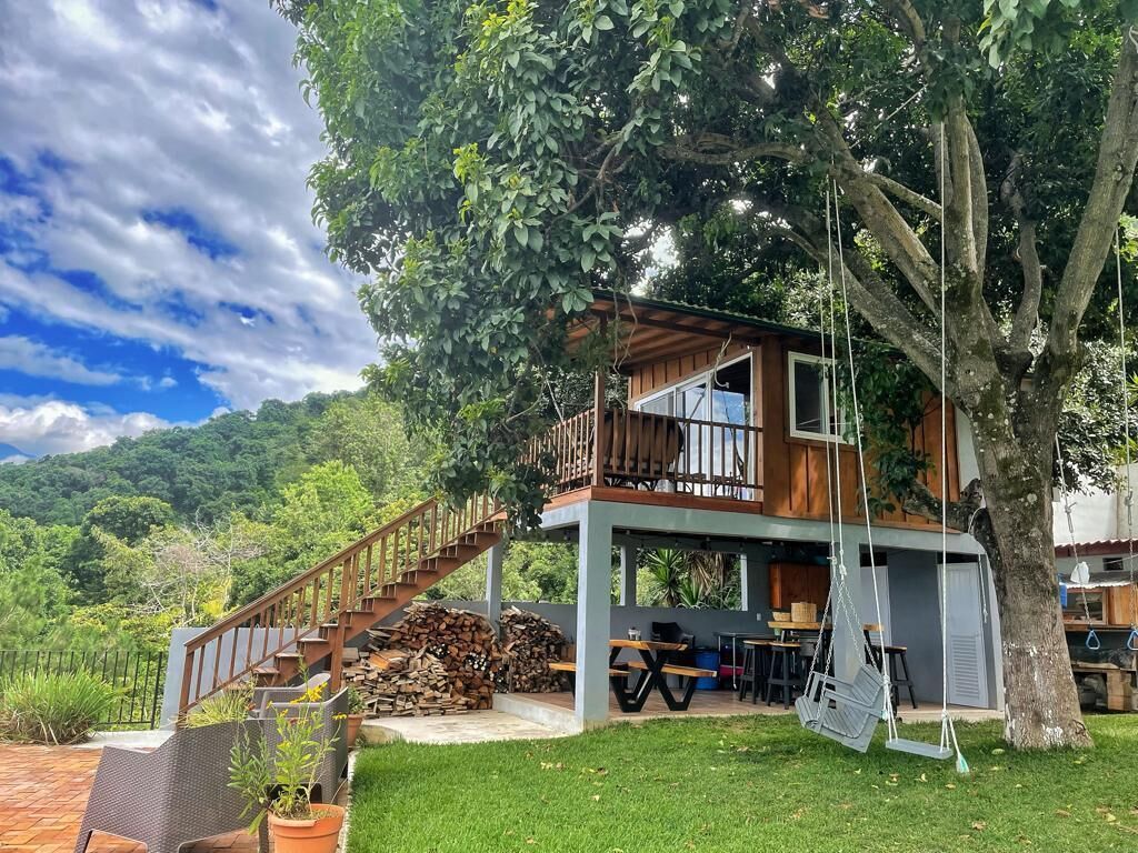 Uma cabana de madeira de dois andares com varanda, escadaria e área de pátio com mobiliário para área externa.