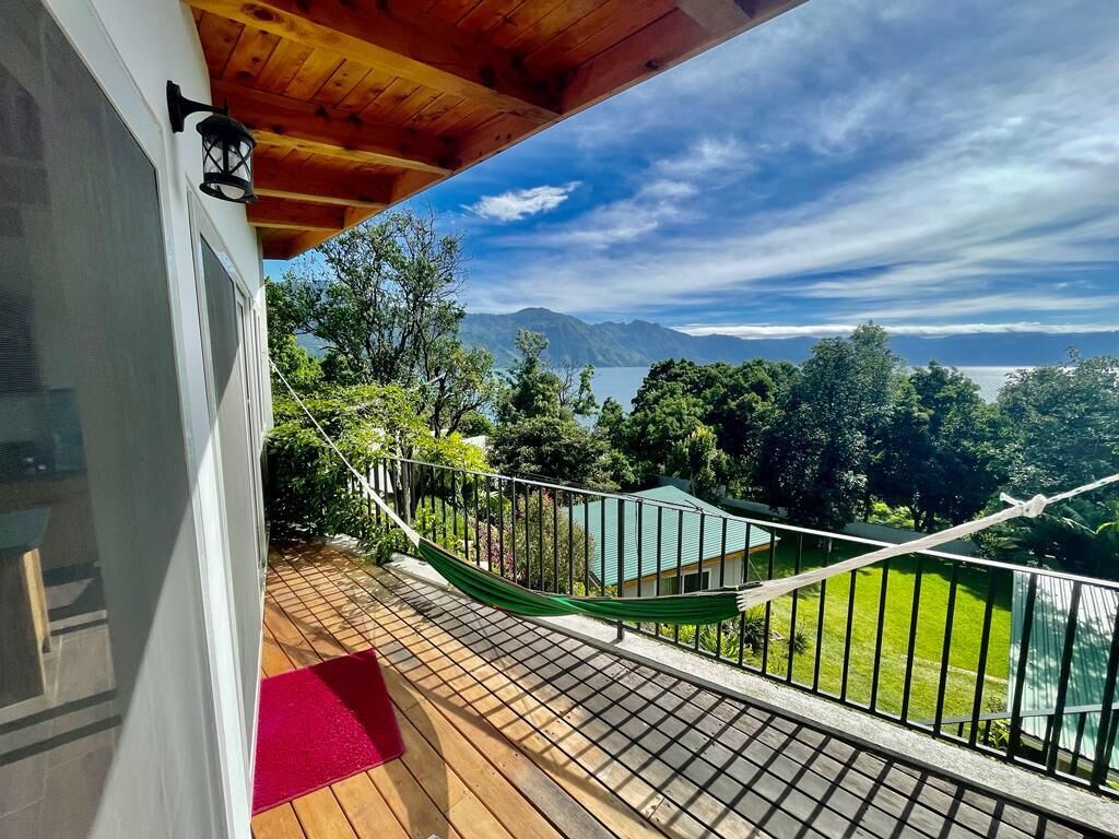 Un balcón con hamaca, suelo de madera y vistas a montañas y follaje.
