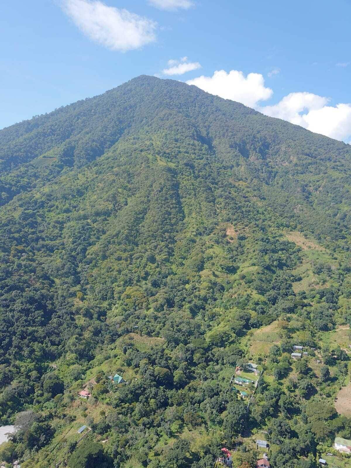 A mountain with dense green vegetation and a few scattered buildings at its base.