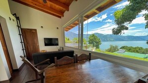 Un comedor con una gran mesa de madera y sillas, un televisor y vistas a un lago y montañas.