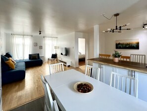 A modern living space with a dining area, a sofa set, a TV, and a painting on the wall. - Large Apartment in Downtown (Québec)