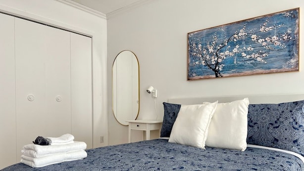 A bedroom with a bed, a nightstand, a mirror, and a painting on the wall. - Large Apartment in Downtown (Québec)