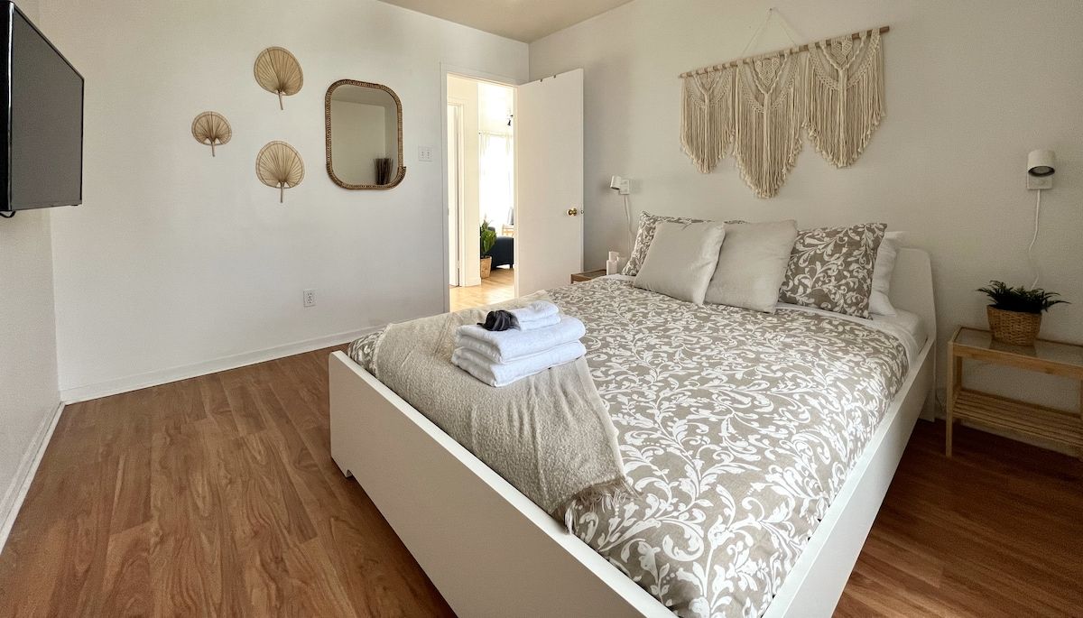 Une chambre à coucher comprenant un lit, une table de chevet, un téléviseur fixé au mur et une porte donnant sur une autre pièce.