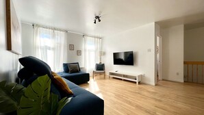 A modern living room with a flat-screen TV, a sofa, a chair, and a large plant. - Large Apartment in Downtown (Québec)