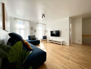 A modern living room with a flat-screen TV, a sofa, a chair, and a large plant. - Large Apartment in Downtown (Québec)