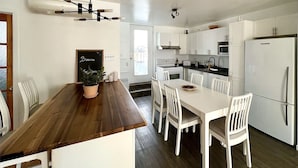 A modern kitchen with white cabinetry, a wooden dining table, and a built-in oven. - Large Apartment in Downtown (Québec)