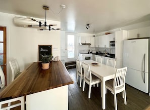 A modern kitchen with white cabinetry, a wooden dining table, and a built-in oven. - Large Apartment in Downtown (Québec)