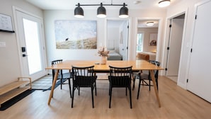 Un comedor con una mesa de madera y sillas negras, un cuadro grande en la pared y un banco junto a la puerta.