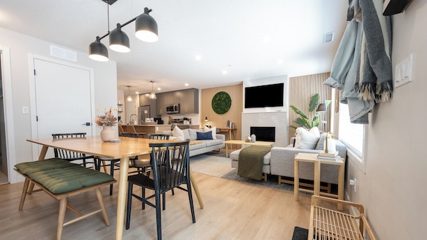Una sala de estar moderna con comedor, una cocina al fondo y un televisor montado en la pared.