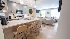 Una cocina moderna con una isla central, taburetes de bar, microondas y un ventanal grande.