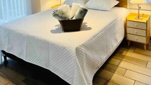 Een netjes opgemaakt bed met hoofdbord, een nachtkastje met lamp en een raam met zonwering.