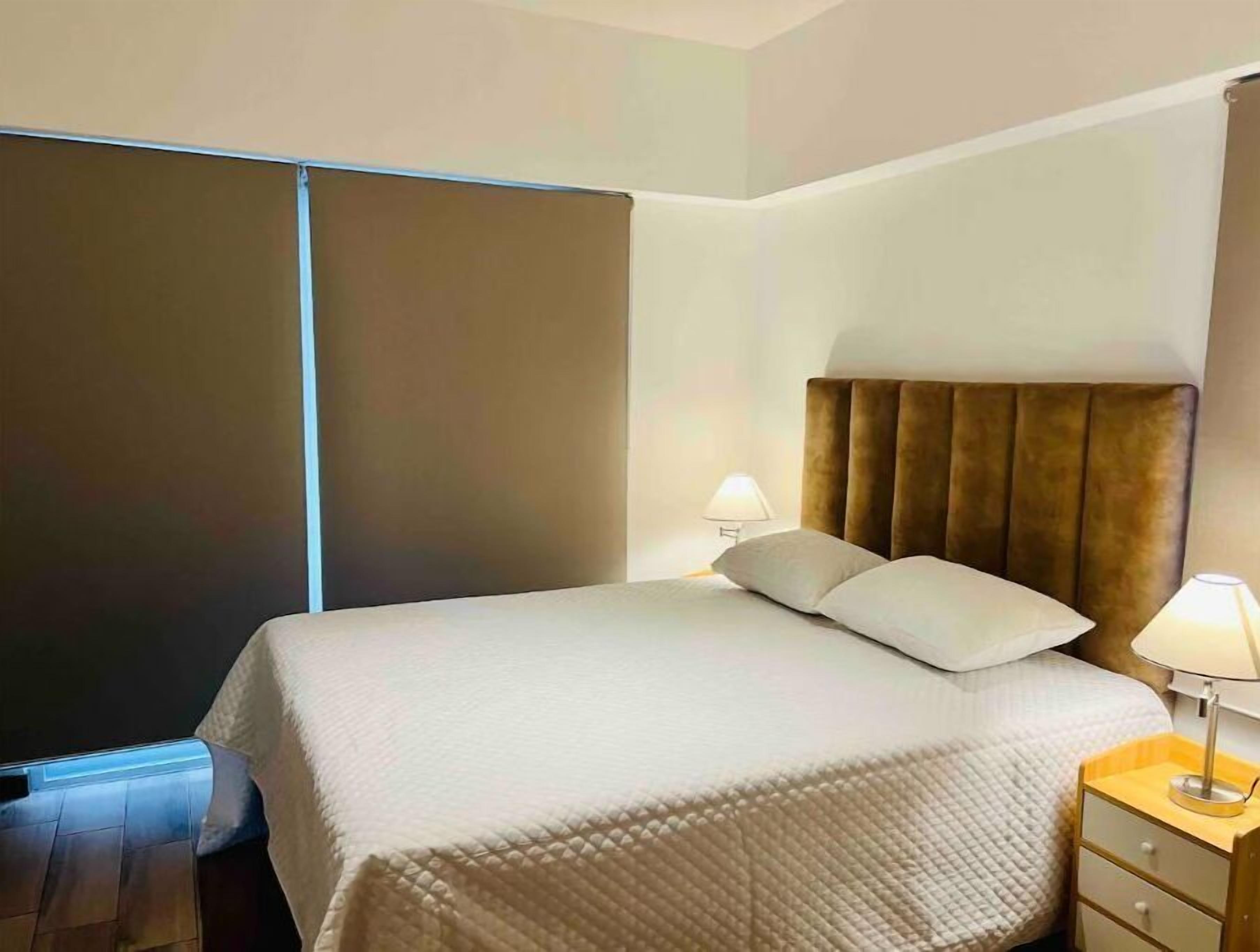 Une chambre d’hôtel avec un lit, des lampes de chevet, une table de chevet en bois et une grande fenêtre.