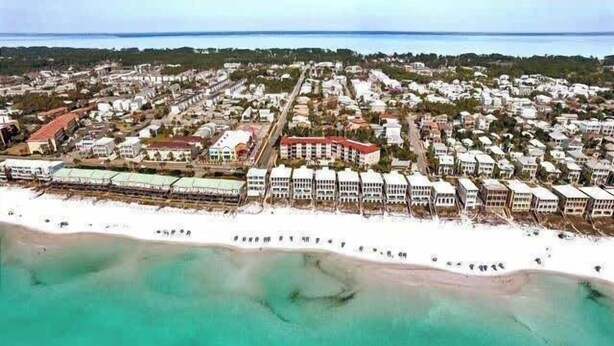 An aerial view of a coastal resort with beachfront villas, a sandy beach, and a clear view of the ocean.