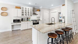 A modern kitchen with white cabinetry, a marble island with bar stools, and a stainless steel range hood.