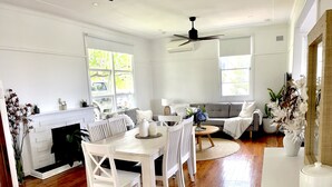Ein geräumiges Wohnzimmer mit Kamin, einer Essecke mit rundem Tisch und Stühlen sowie einer Sitzecke mit Sofa und Sesseln.