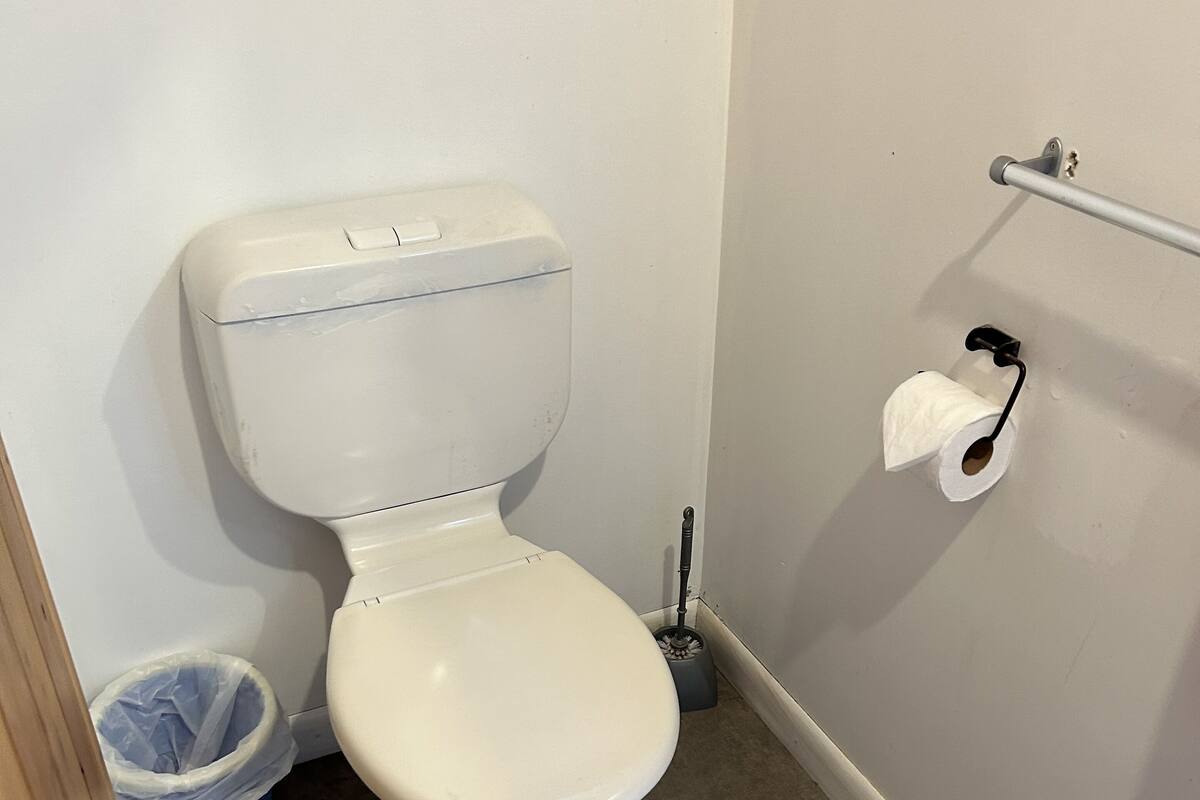 Des toilettes blanches avec un porte-serviettes en papier fixé au mur, une poubelle bleue et un balai.