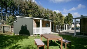 Un petit bâtiment d’un seul étage, doté d’un porche clôturé, d’une table en bois et de deux bancs, le tout situé dans une cour verdoyante.