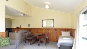 Une pièce compacte comprenant un coin cuisine, un espace repas avec une table et des chaises, un lit avec un oreiller et un miroir au mur.