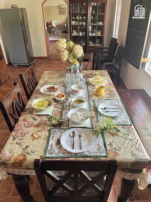 Una mesa de comedor dispuesta con diversos platos, un florero con flores y una cocina al fondo.