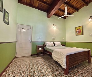 Un dormitorio con cama, mesita de noche, ventilador de techo, una puerta y baldosas de suelo estampadas.