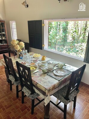 Un comedor con una mesa dispuesta para cuatro, sillas, una ventana con vistas a la vegetación y un aparador con vajilla.