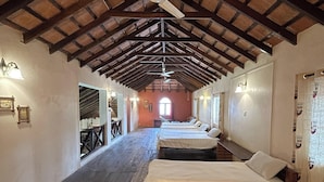 Una habitación de hotel con un techo de madera alto, un ventilador de techo y una fila de camas.