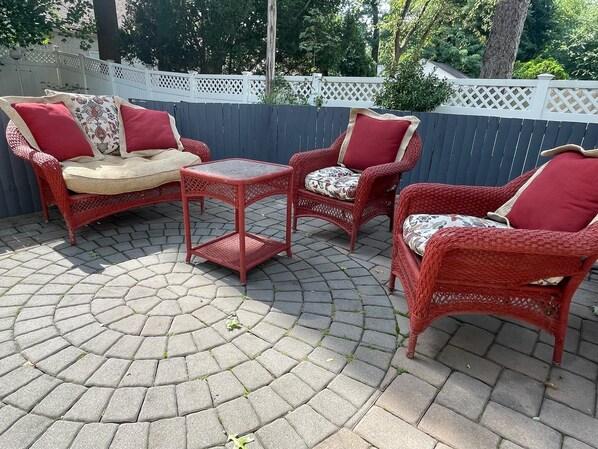A patio area with wicker furniture, including a sofa, two chairs, and a small table, arranged on a paved surface. - New Jersey home, close to NY City Fun! (Englewood)