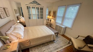 Een slaapkamer met een bed, nachtkastje, lamp, stoel en een groot raam met zonwering.