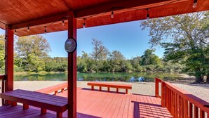 Une terrasse en bois avec des bancs, donnant sur un lac paisible, le tout entouré d’arbres.