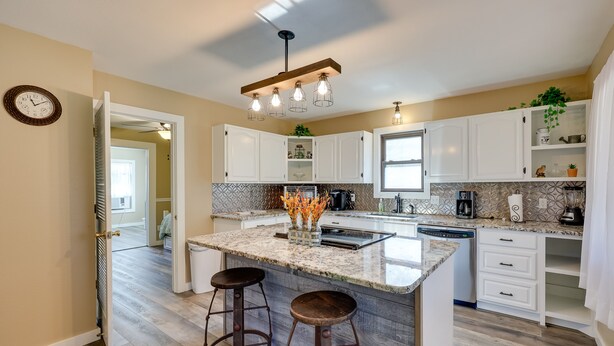 Une cuisine moderne avec des meubles blancs, un grand îlot central doté de tabourets et un luminaire suspendu.