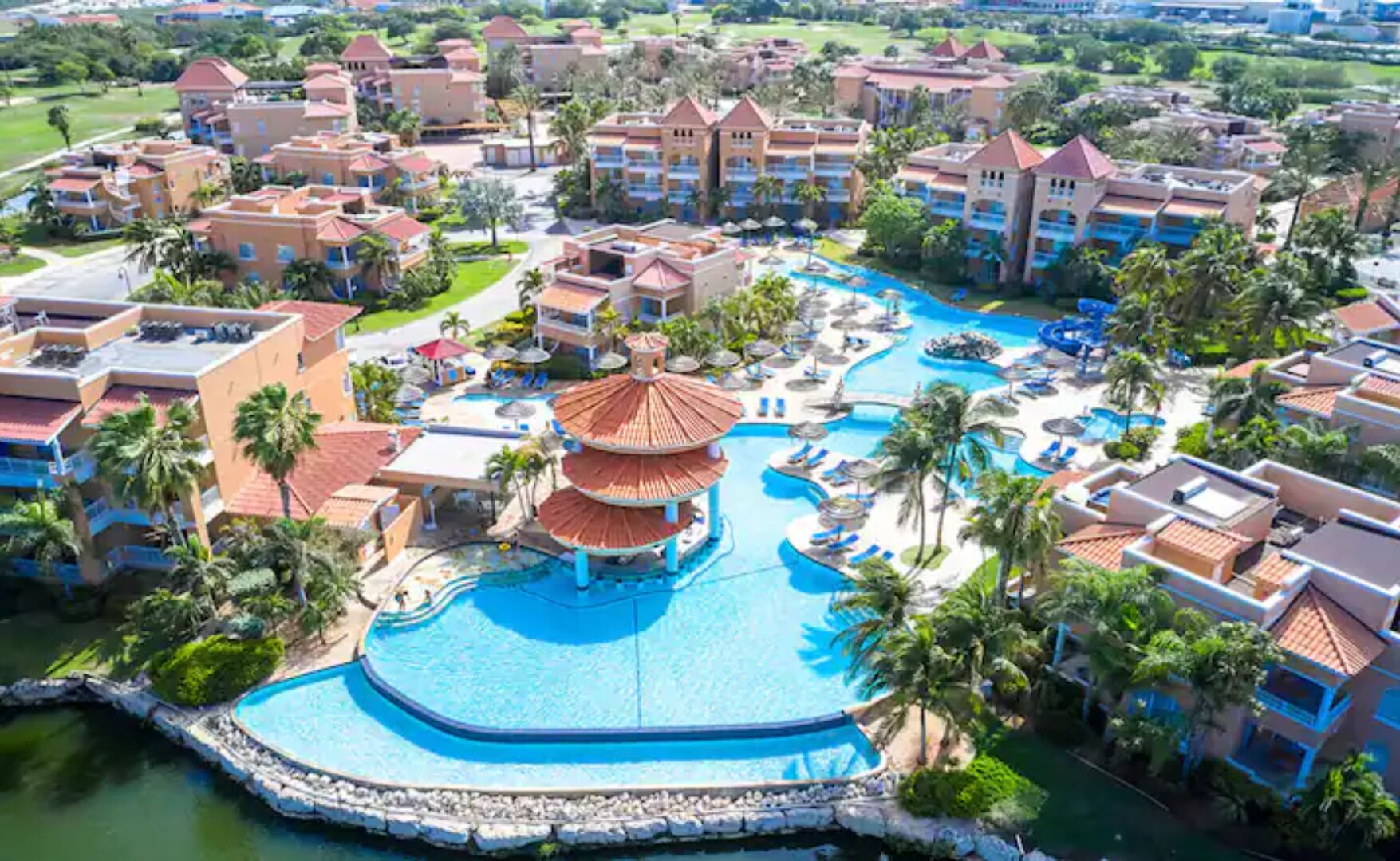 Een resort met een centraal zwembad, meerdere gebouwen en palmbomen.