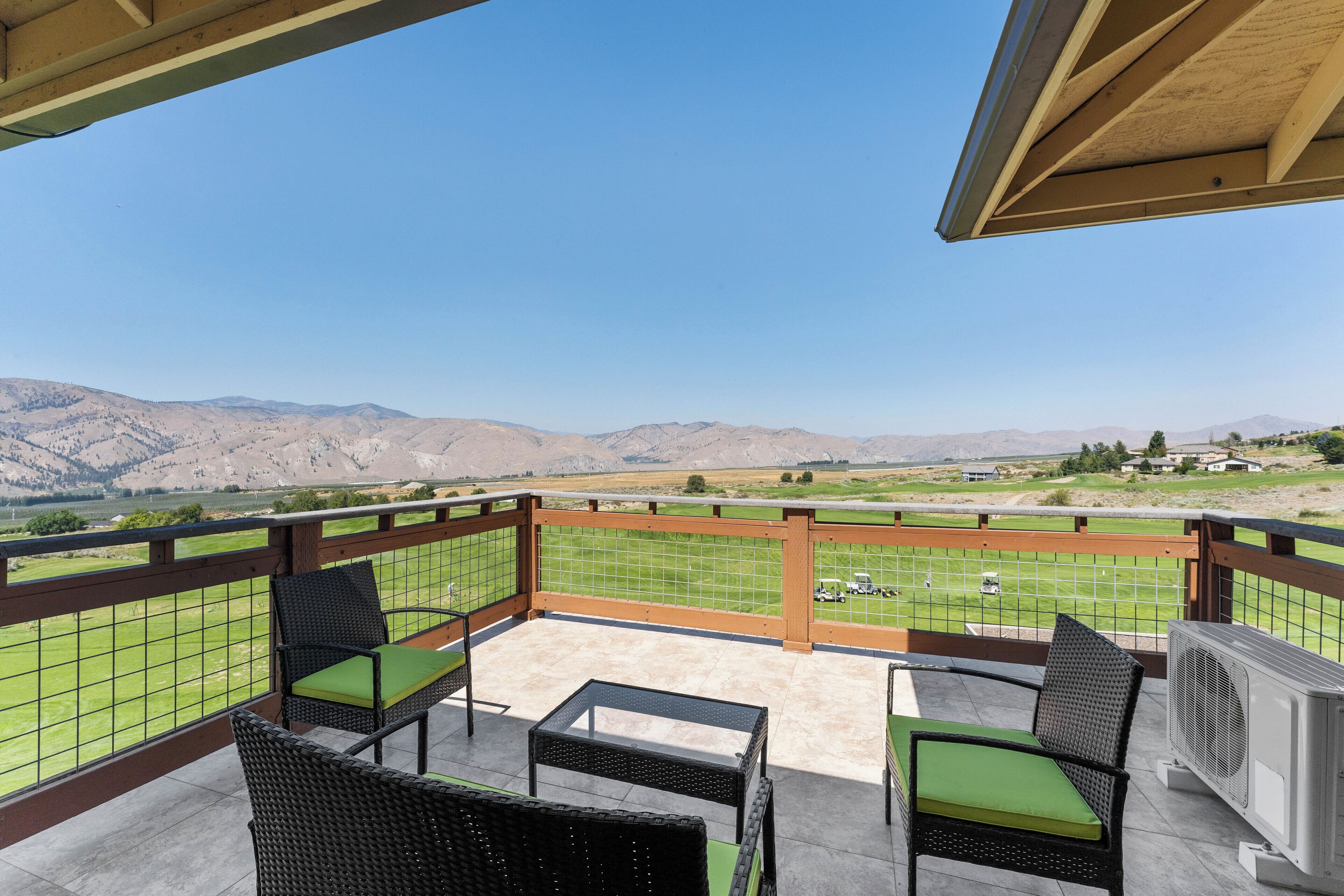 Un balcón con mobiliario de mimbre y vistas a un campo de golf y montañas.