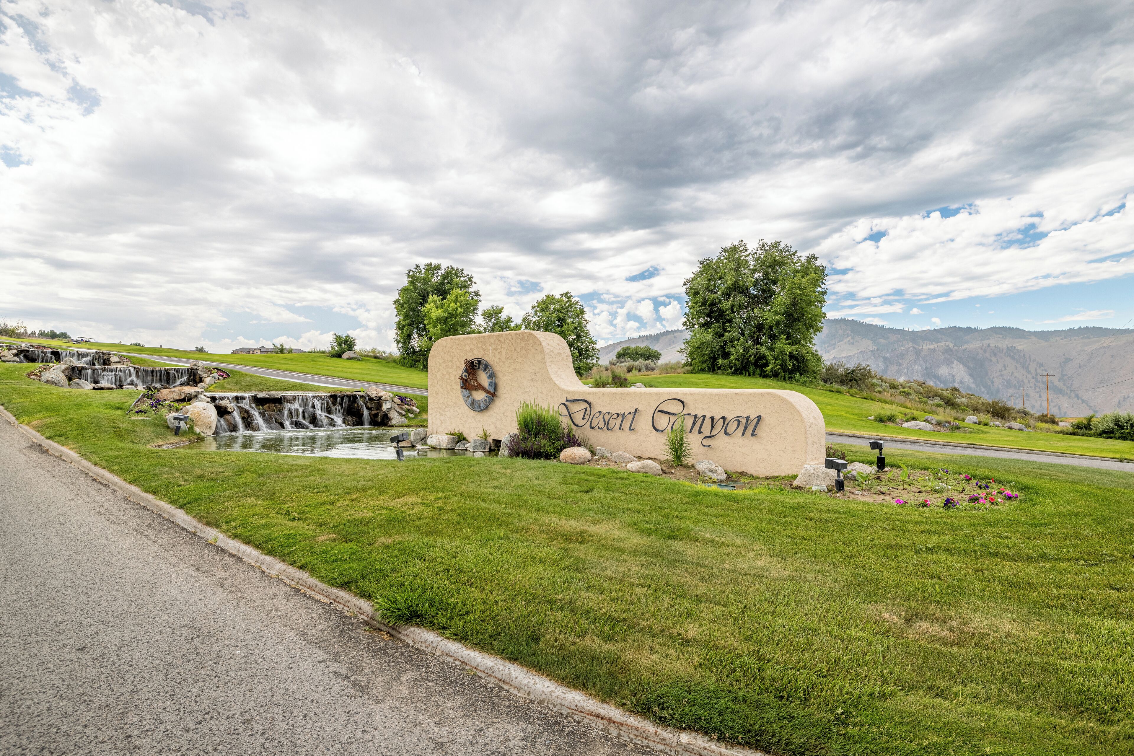A desert-themed sign with a waterfall, surrounded by green grass and trees.