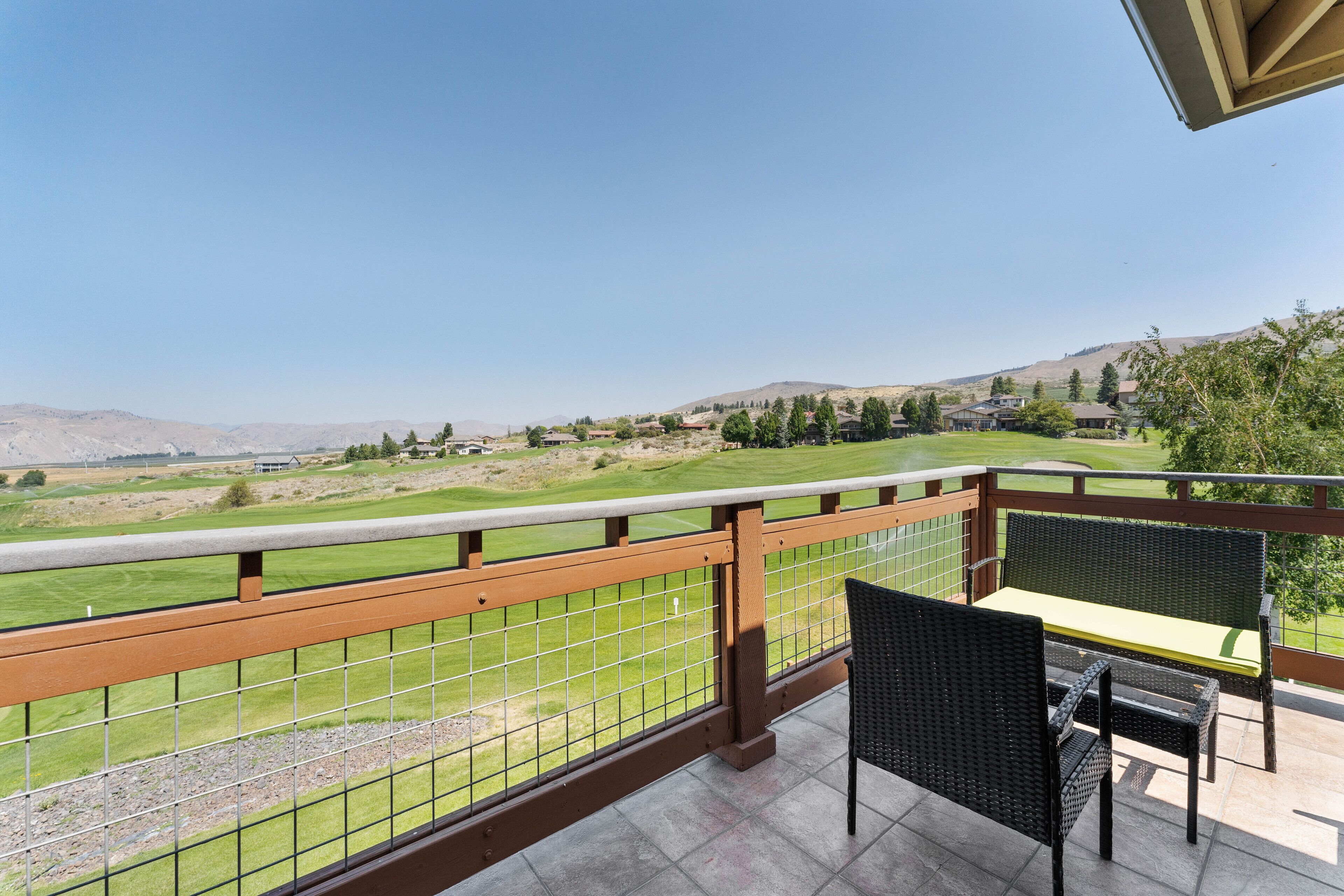 A balcony with a view of a golf course, a wicker chair, and a table.
