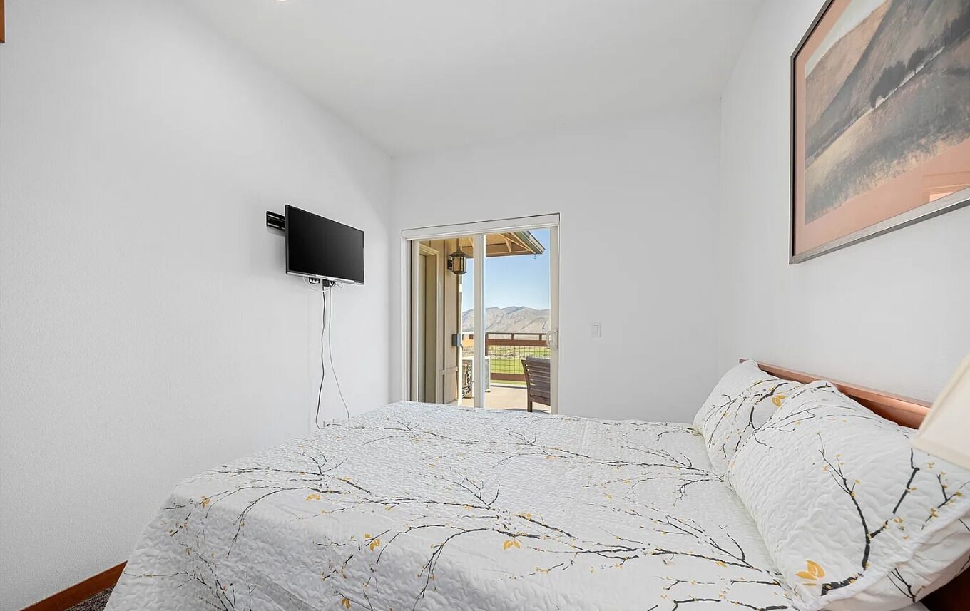 Une chambre à coucher avec un lit, un téléviseur fixé au mur et une porte donnant sur un balcon.