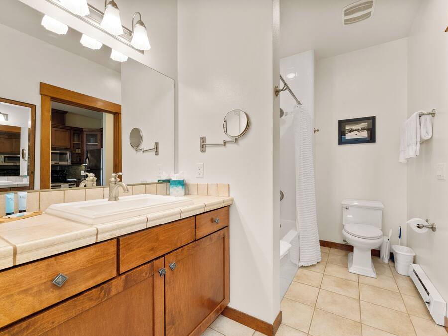 A bathroom with a wooden vanity, a large mirror, a toilet, and a shower area.