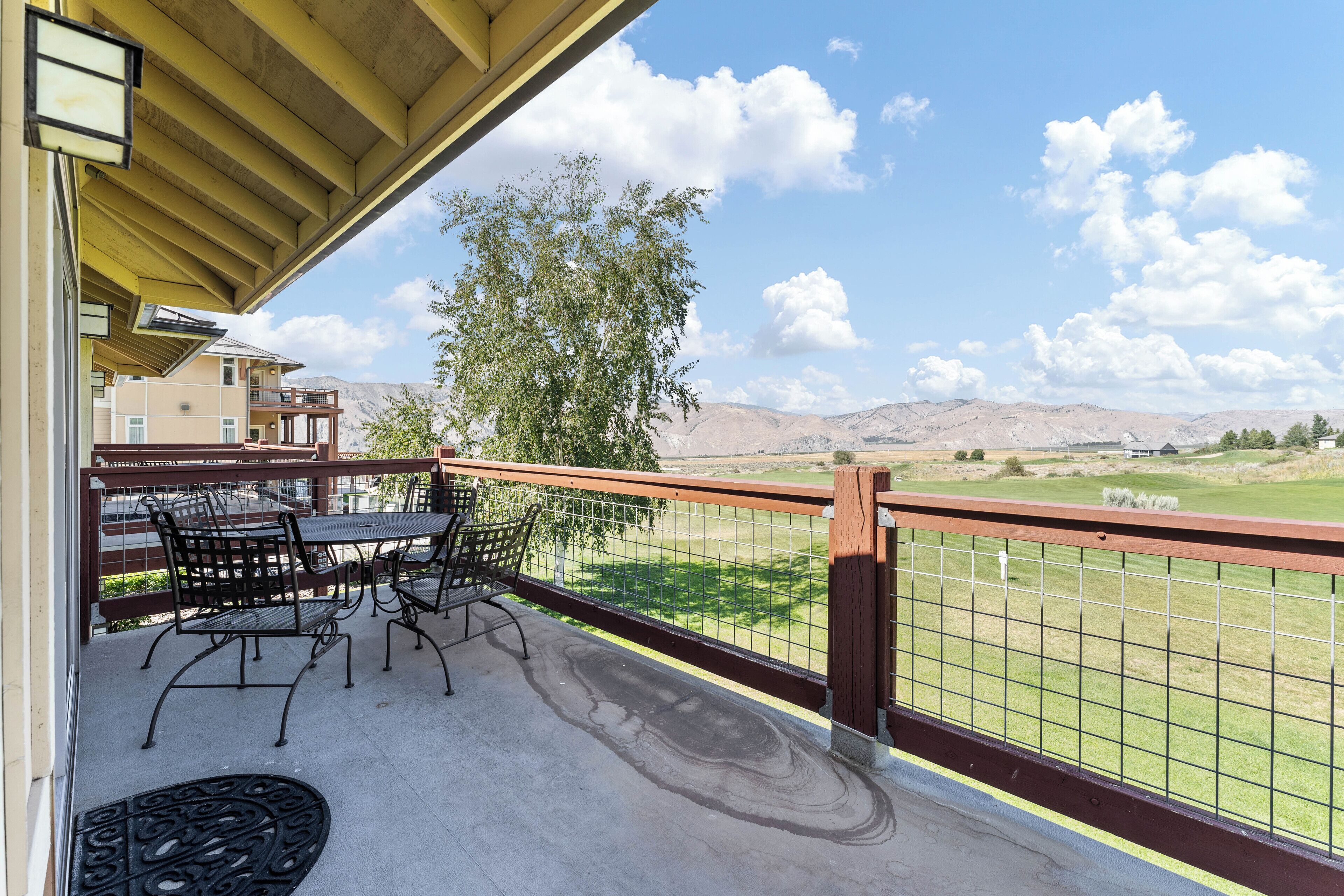 A balcony with a table and chairs, overlooking a grassy area and mountains.